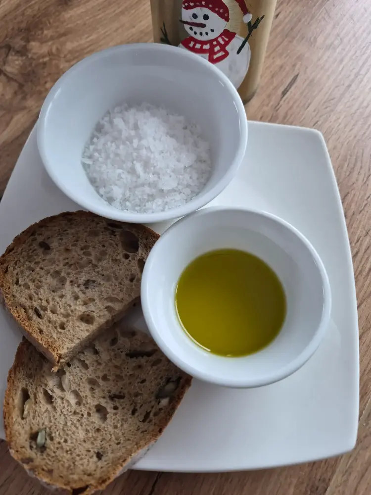 Extra virgin olive oil from West Mani Greece in a white bowl with bread and sea salt on a plate.