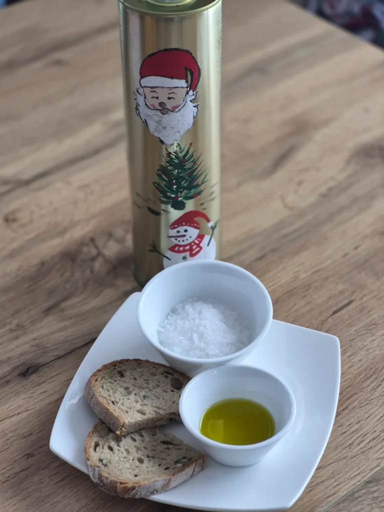 extra virgin olive oil from West Mani Greece in a white bowl - it has a beautiful green colour, on the same plate there are slices of fresh bread and some sea salt, in the background a Christmas decorated tin